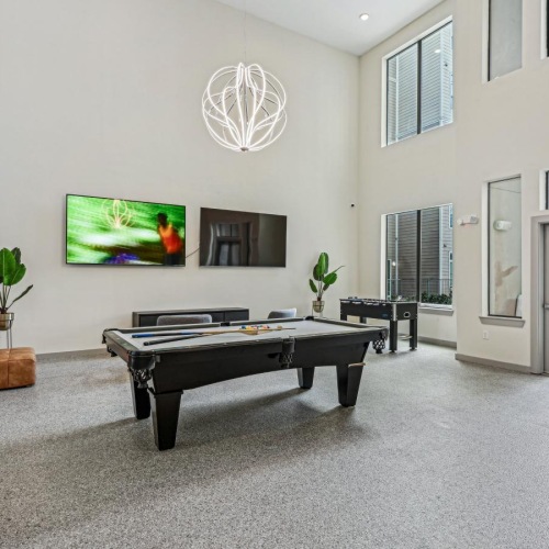 a room with a pool table and chairs and two tv's